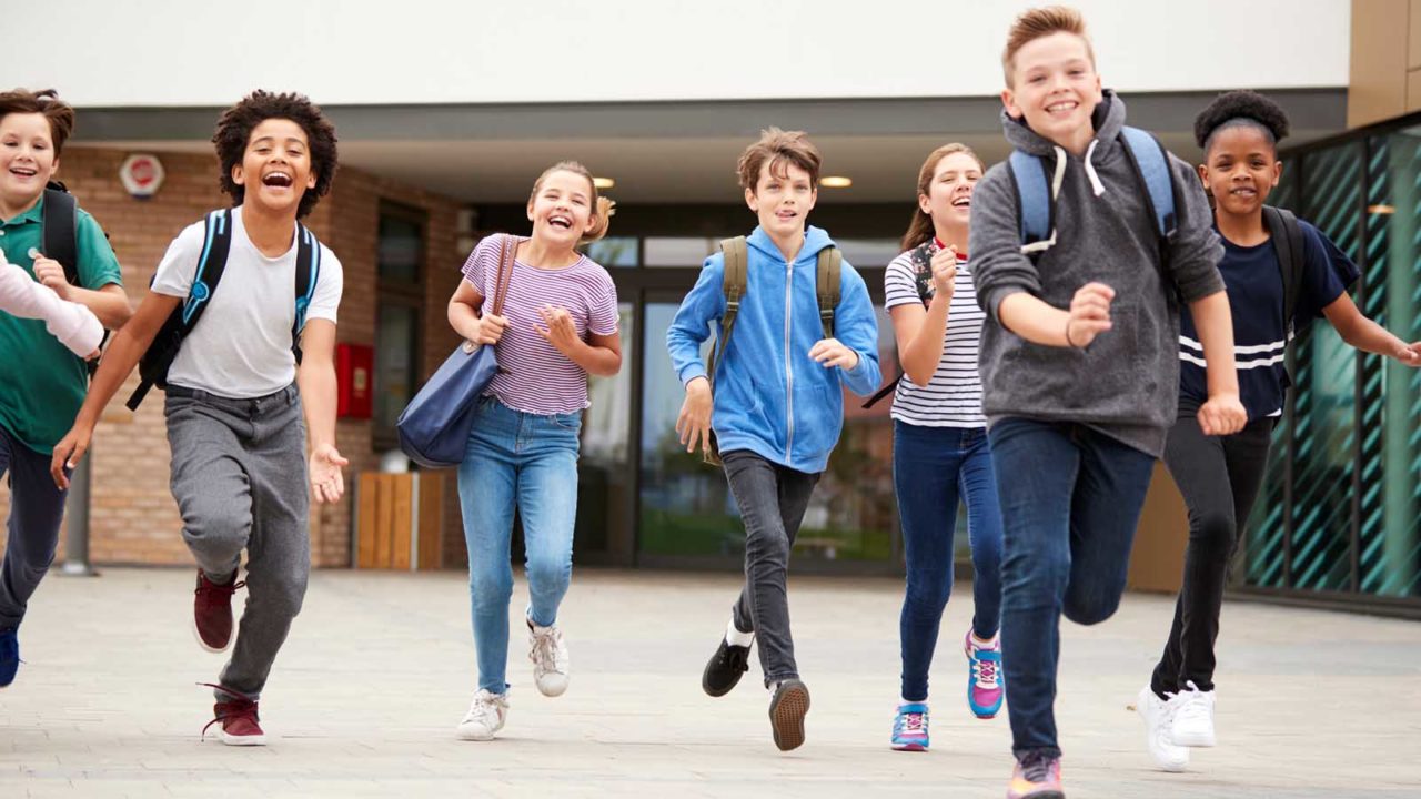 Foto: Shutterstock. Bildet viser skoleelever som løper ut fra en skolebygning, de er glade.
