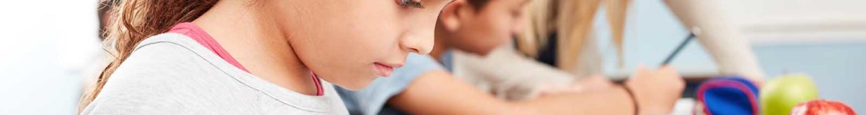 Foto: Shutterstock. Jente sitter med mobiltelefon ved pulten i klasserommet. Lærer i bakgrunnen.