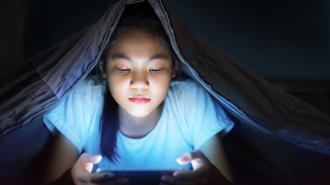 Foto: Shutterstock. Bildet viser et barn med nettbrett i et mørkt rom.