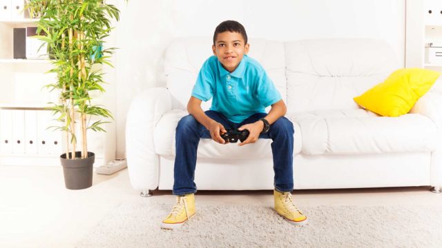 Foto: Shutterstock. Bildet viser en gutt som sitter foroverlent i en sofa og spiller dataspill.