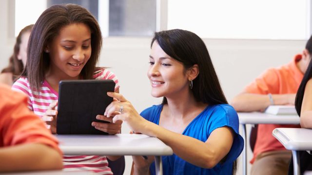 Foto: Shutterstock. Bilde viser en lærer som hjelper en elev med nettbrett.