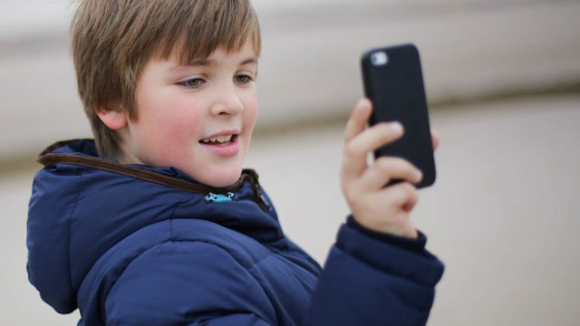 Foto: Shutterstock. Bildet viser en gutt i vinterjakke som holder opp en telefon for å ta et bilde.