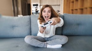 Foto: Shutterstock. Bildet viser ei jente med spillkontroller. Hun sitter i en sofa i en stue og er svært engasjert i spillingen.