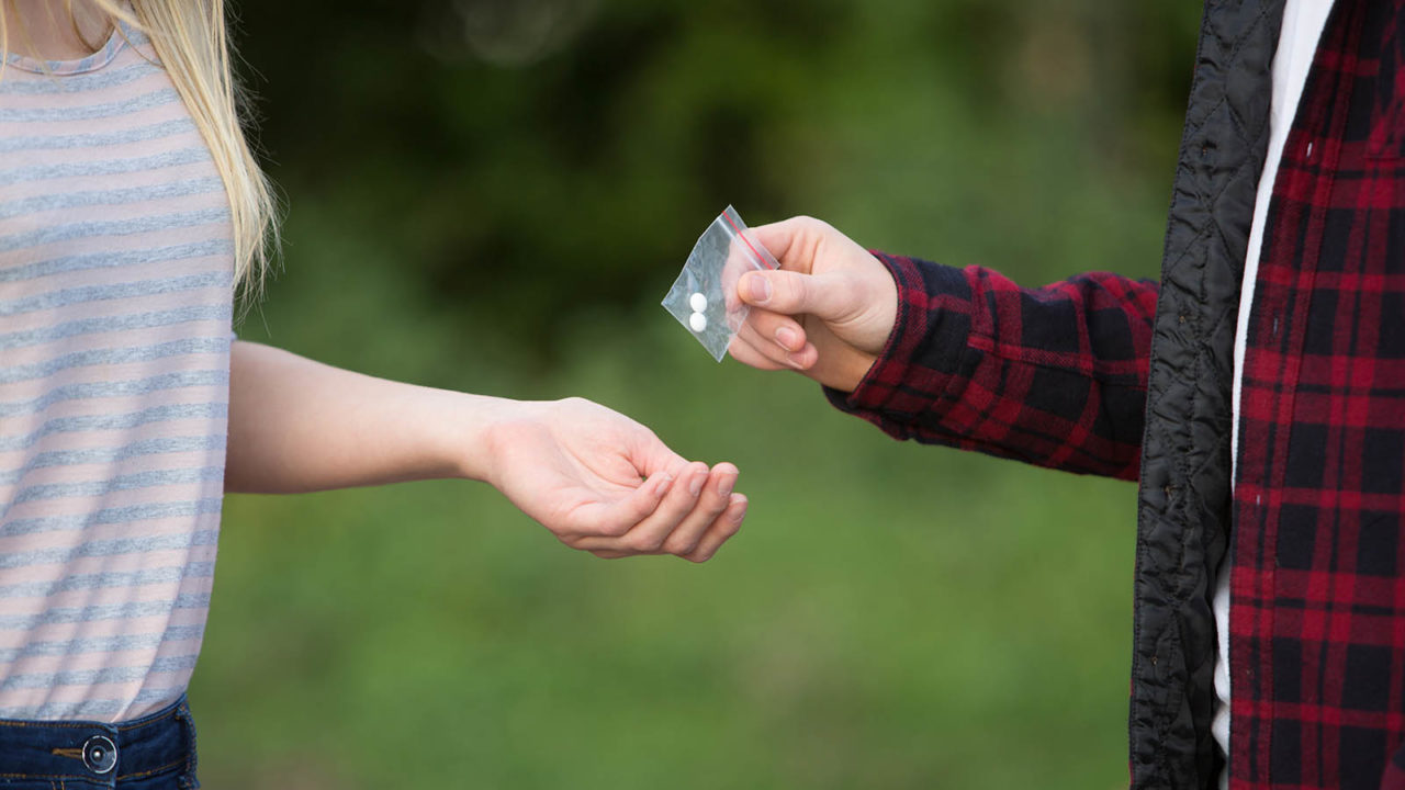 Foto: Shutterstock / Daisy Daysi. Bildet viser en tenåringsjente som kjøper tabletter av en ung mann.