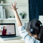 Foto: Shutterstock / Hananeko_Studio. Bildet viser ei jente som rekker opp hånden. Hun sitter hjemme og følger undervisning på skjerm.