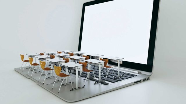 Foto: Shutterstock / creo2. Bildet viser en datamaskin hvor det er plassert skolepulter og stoler i miniatyr oppå tastaturet.