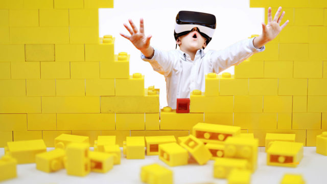 Foto: Shutterstock / Lewis Tse Pui Lung / SOK Studio / Barnevakten. Bildet viser en gutt med VR-briller, han presser seg gjennom en mur med legoklosser.