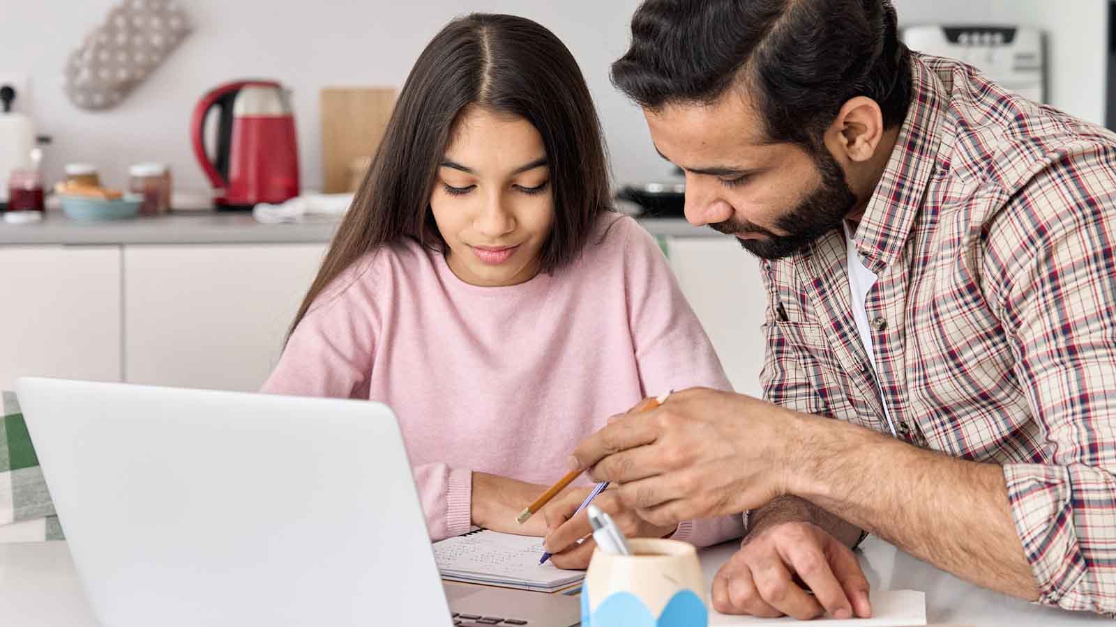 Foto: Shutterstock / insta_photos. Bildet viser en pappa som hjelper sin dateter med leksene, på bordet er en PC.