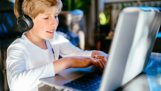 Foto: Shutterstock / Iryna Inshyna. En gutt sitter hjemme med hodetelefoner og jobber på datamaskin.