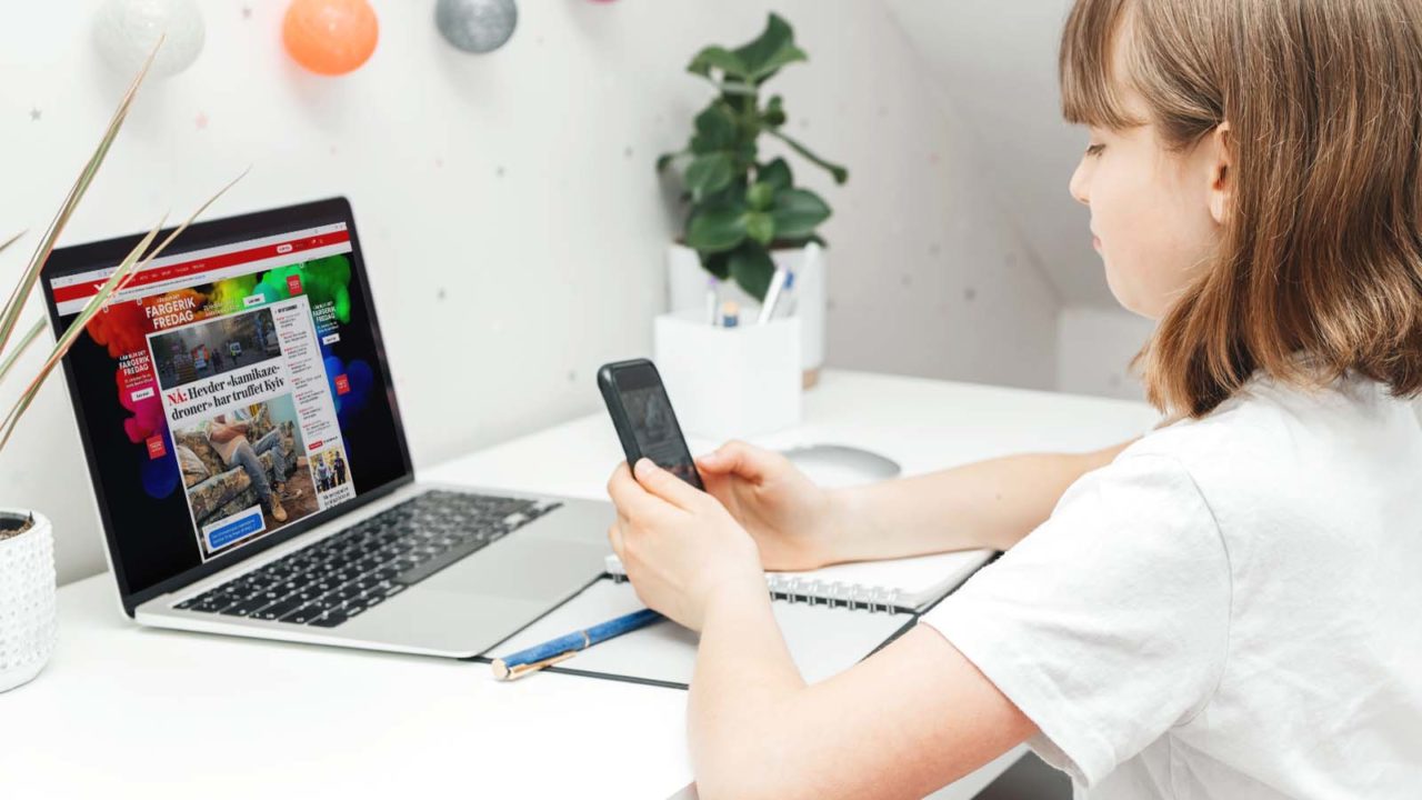 Foto: Shutterstock / Elena Medoks / Barnevakten. Bilde viser ei jente på rommet sitt, hun ser på nyheter på mobil og PC.