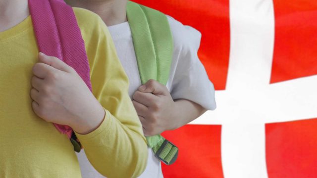 Foto: Shutterstock / lunopark. Bildet viser to elever med skolesekk, i bakgrunnen det danske flagget.