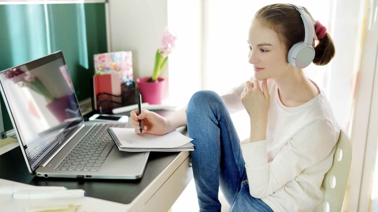 Foto: Shutterstock / MNStudio. Bildet viser ei jente som sitter ved PC-en ved pulten hjemme.