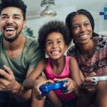 Foto: Shutterstock / adriaticfoto. Bildet viser en familie som gamer sammen hjemme i stua.