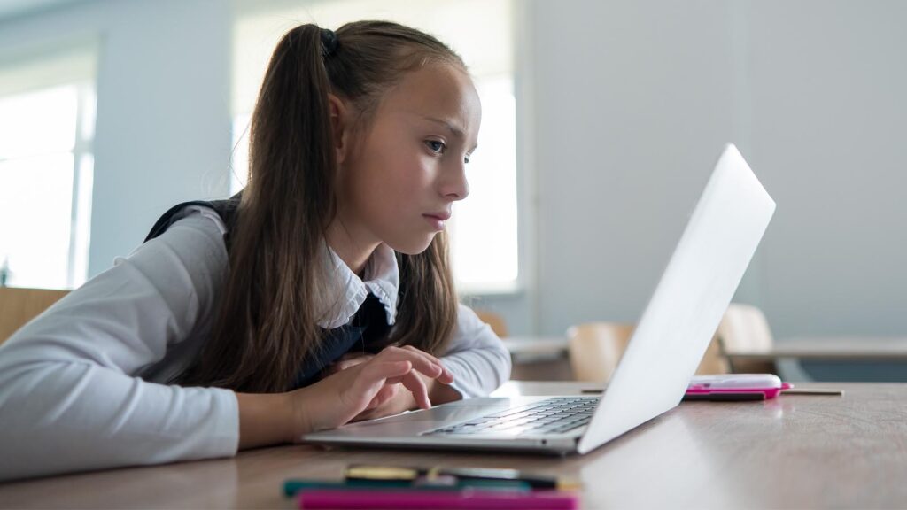 Foto: Shutterstock / Reshetnikov_art. Bildet viser ei jente som ser på en skjerm i et klasserom.