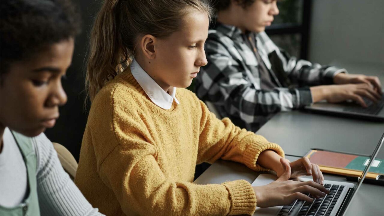 Foto: Shutterstock / AnnaStills. Bildet viser tre elever med hver sin datamaskin.